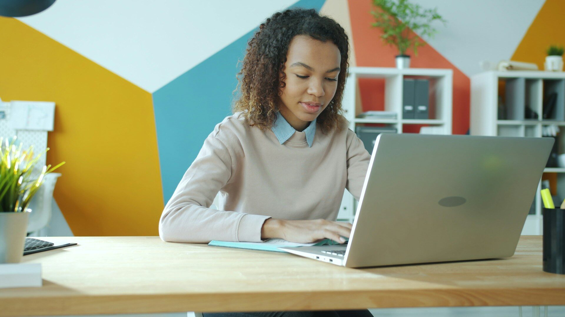 Junge Frau sitzt lächelnd an einem Schreibtisch und arbeitet an einem Laptop